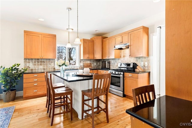 kitchen featuring gas stove, hanging light fixtures, light hardwood / wood-style flooring, a kitchen breakfast bar, and a kitchen island