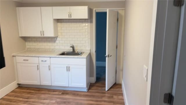 kitchen with tasteful backsplash, hardwood / wood-style flooring, sink, and white cabinets