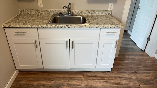 kitchen with white cabinetry, sink, light stone counters, and dark wood-type flooring