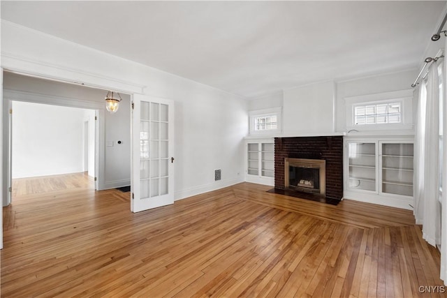 unfurnished living room featuring built in shelves, a healthy amount of sunlight, a fireplace, and light wood-type flooring