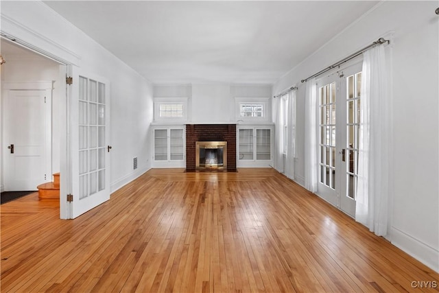 unfurnished living room featuring a brick fireplace, hardwood / wood-style floors, and french doors