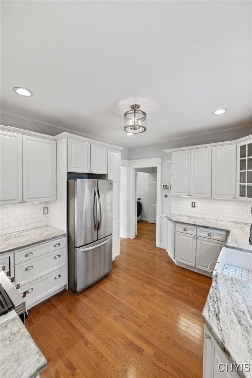 kitchen featuring stainless steel refrigerator, white cabinetry, decorative backsplash, light stone countertops, and light wood-type flooring