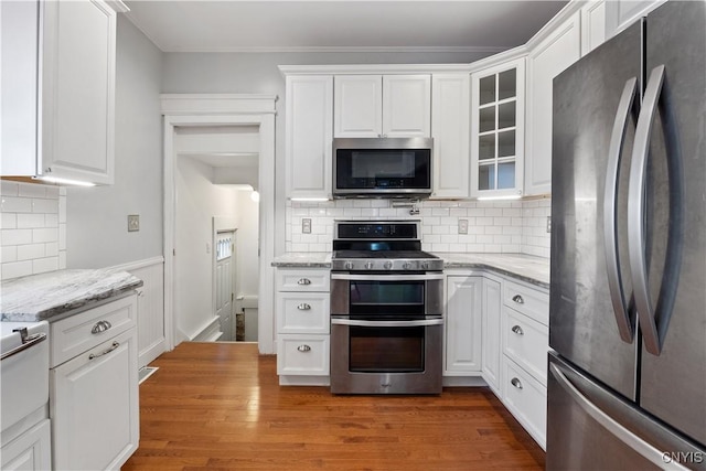 kitchen with light stone counters, appliances with stainless steel finishes, tasteful backsplash, and white cabinets