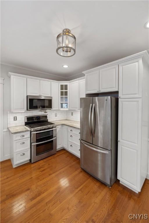 kitchen featuring crown molding, white cabinetry, stainless steel appliances, tasteful backsplash, and light wood-type flooring