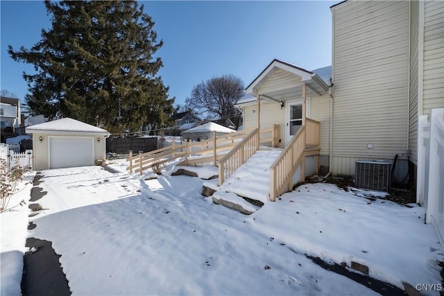 yard layered in snow featuring a garage, an outdoor structure, and central AC unit