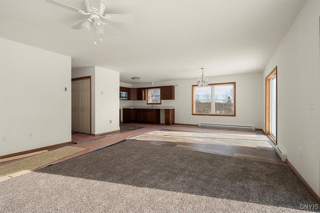 unfurnished living room featuring ceiling fan with notable chandelier, dark carpet, and a baseboard heating unit