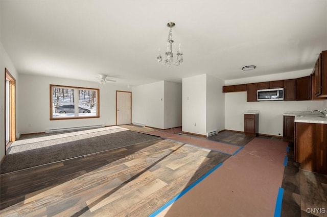 unfurnished living room with baseboard heating, ceiling fan with notable chandelier, and sink