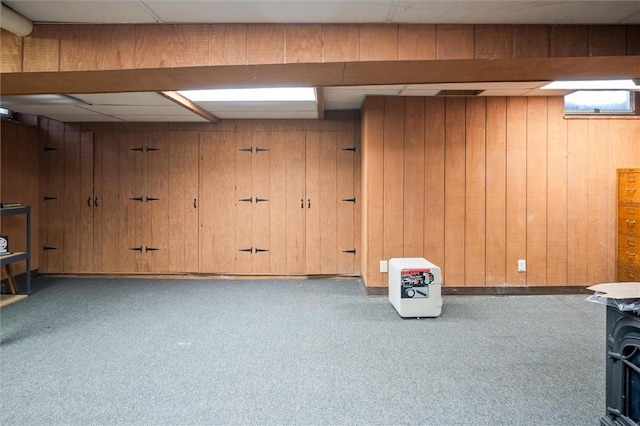 basement with a paneled ceiling, light colored carpet, and wood walls