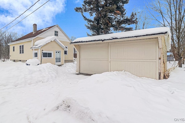 snow covered property with a garage and an outdoor structure