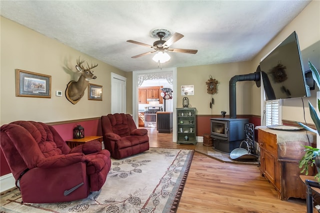 living room featuring a textured ceiling, light hardwood / wood-style flooring, ceiling fan, and a wood stove