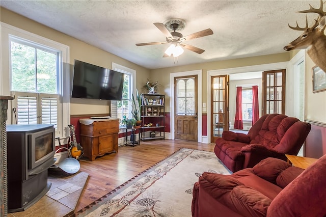 living room featuring ceiling fan, light hardwood / wood-style flooring, a textured ceiling, and a wood stove