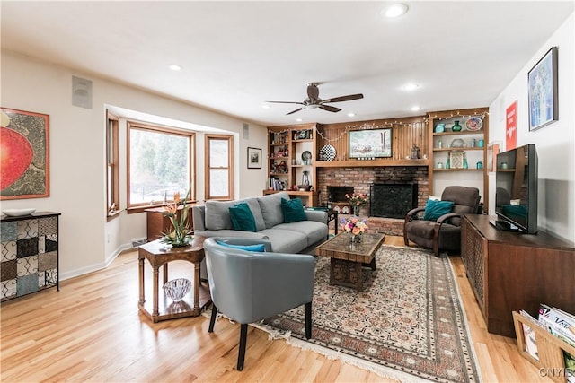 living room with a brick fireplace, built in features, ceiling fan, and light hardwood / wood-style flooring