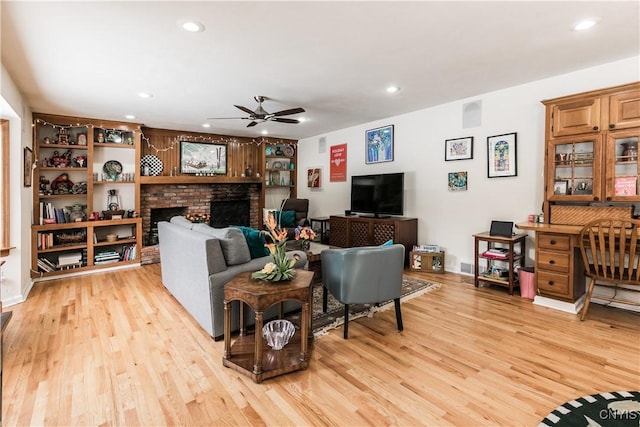 living room with a brick fireplace, light hardwood / wood-style floors, and ceiling fan