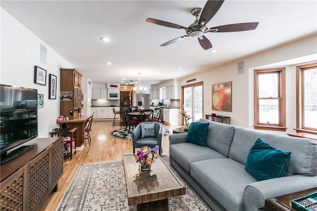 living room featuring ceiling fan with notable chandelier and light wood-type flooring