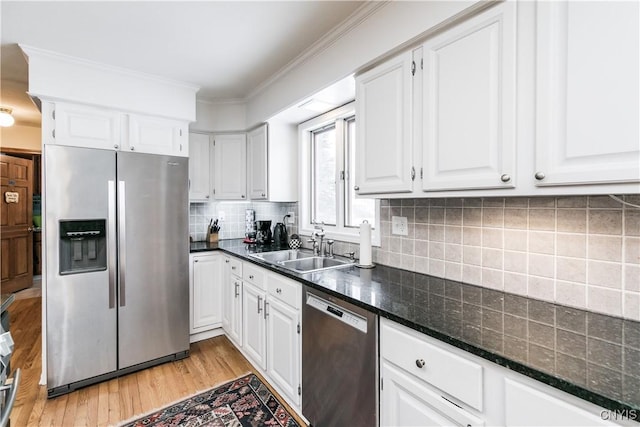 kitchen with appliances with stainless steel finishes, tasteful backsplash, sink, white cabinets, and light wood-type flooring