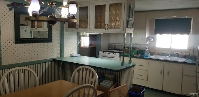 kitchen with sink, white range with gas stovetop, hanging light fixtures, extractor fan, and white cabinets