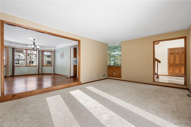 spare room with crown molding, carpet flooring, and an inviting chandelier