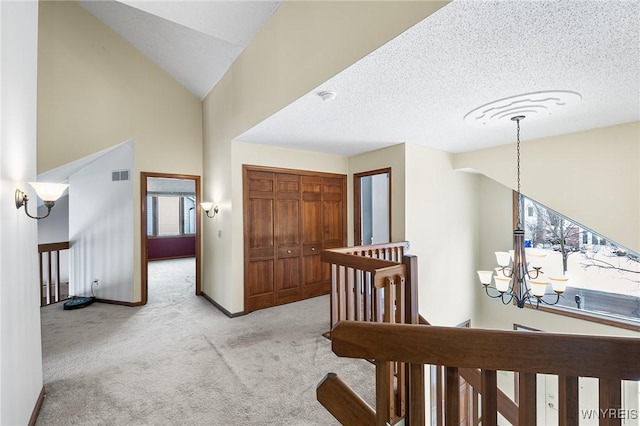 hall with vaulted ceiling, light colored carpet, a textured ceiling, and a chandelier