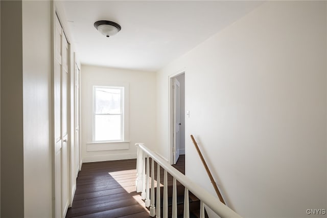 corridor with baseboards, an upstairs landing, and dark wood-style floors