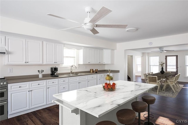 kitchen with a kitchen breakfast bar, dark wood-style floors, a ceiling fan, stove, and a sink