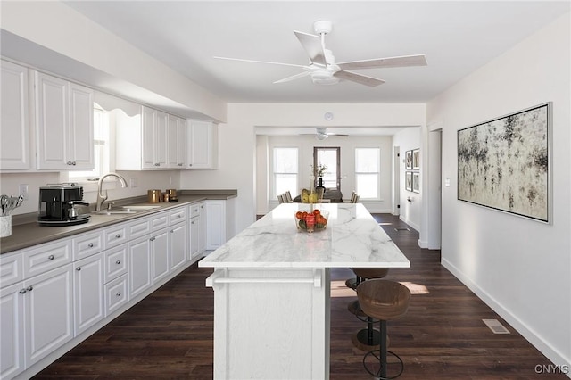 kitchen featuring a breakfast bar, white cabinetry, sink, a center island, and light stone counters