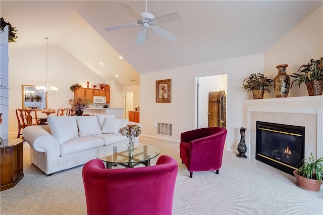 living room featuring ceiling fan with notable chandelier, light colored carpet, vaulted ceiling, and a tile fireplace