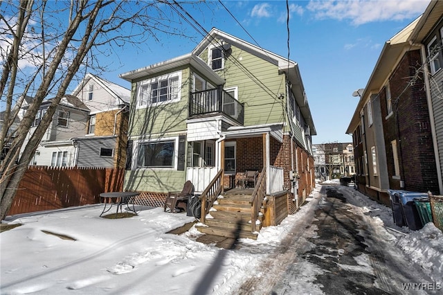 snow covered back of property with a balcony