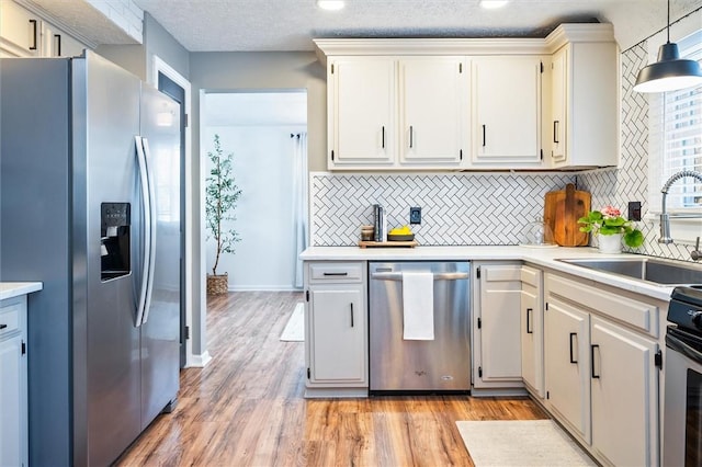 kitchen featuring appliances with stainless steel finishes, pendant lighting, white cabinetry, sink, and backsplash