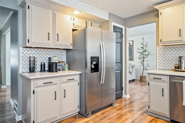 kitchen with appliances with stainless steel finishes, light hardwood / wood-style floors, decorative backsplash, and a textured ceiling