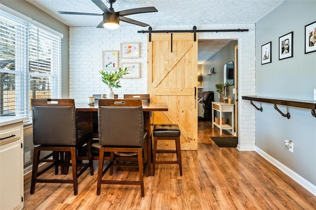 dining area with ceiling fan, light hardwood / wood-style floors, a textured ceiling, brick wall, and a barn door