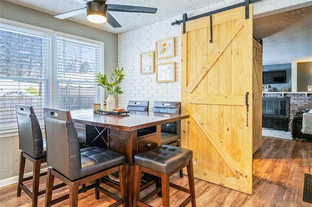 dining area with hardwood / wood-style floors, a barn door, ceiling fan, and brick wall