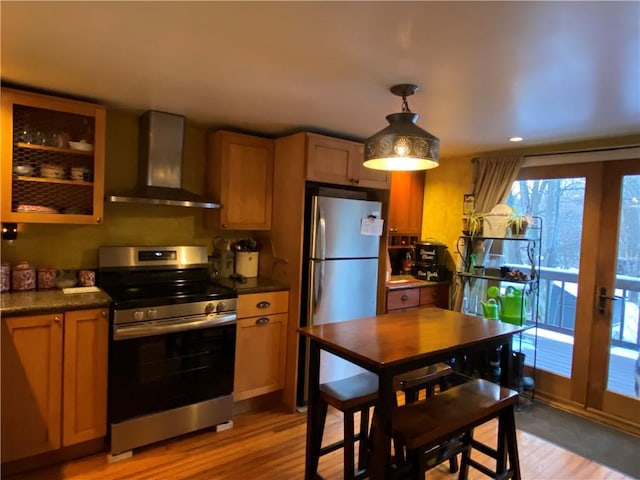 kitchen with hanging light fixtures, appliances with stainless steel finishes, light wood-type flooring, and wall chimney exhaust hood