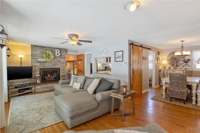 living room featuring a fireplace, wood-type flooring, a barn door, and ceiling fan