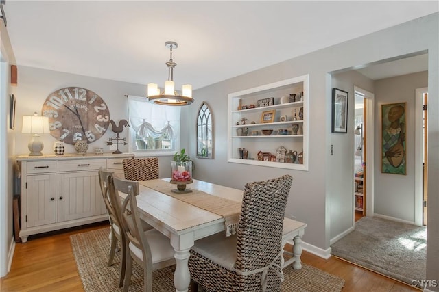 dining area featuring built in shelves, a chandelier, and light hardwood / wood-style floors