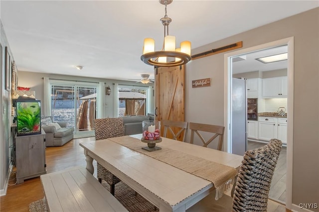 dining space with light hardwood / wood-style flooring, a barn door, and a chandelier