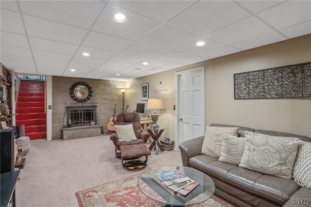 living room featuring a drop ceiling, a stone fireplace, and carpet flooring