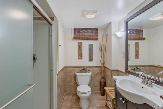 bathroom with a shower with door, tile walls, vanity, tile patterned floors, and toilet