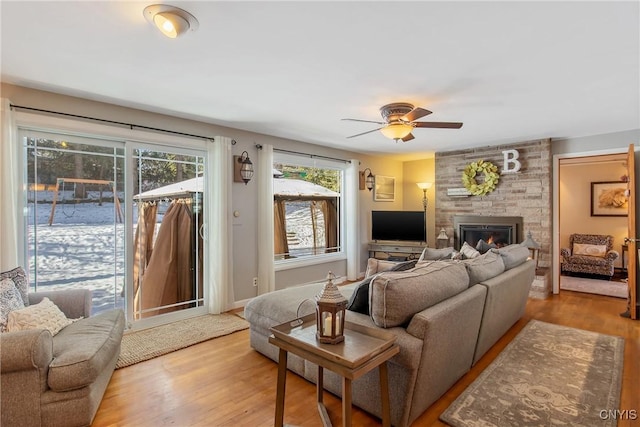 living room with a large fireplace, ceiling fan, and light wood-type flooring