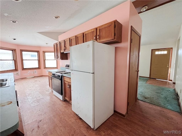 kitchen with a textured ceiling, white appliances, light countertops, brown cabinets, and light wood finished floors