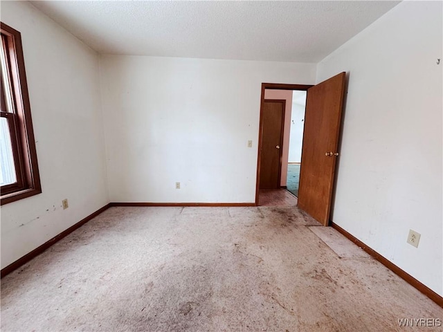 unfurnished room featuring light carpet, a textured ceiling, and baseboards