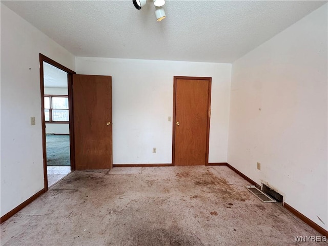 spare room featuring a textured ceiling, visible vents, and baseboards