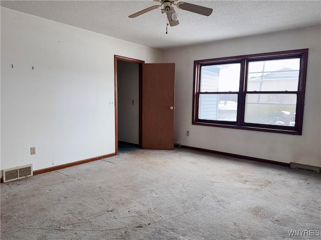 spare room with ceiling fan, a textured ceiling, light carpet, visible vents, and baseboards