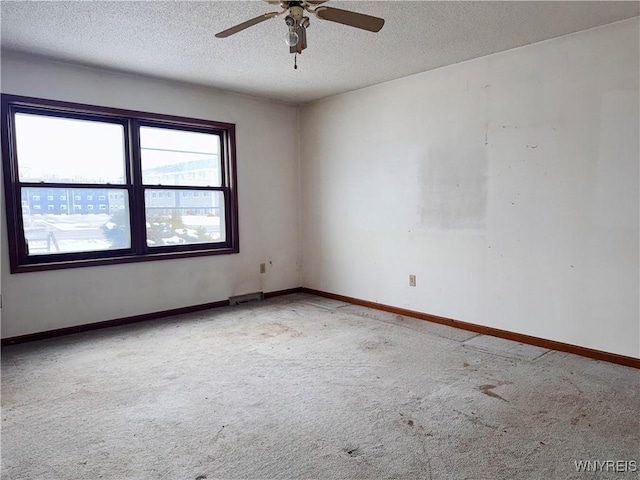 empty room with carpet floors, ceiling fan, baseboards, and a textured ceiling