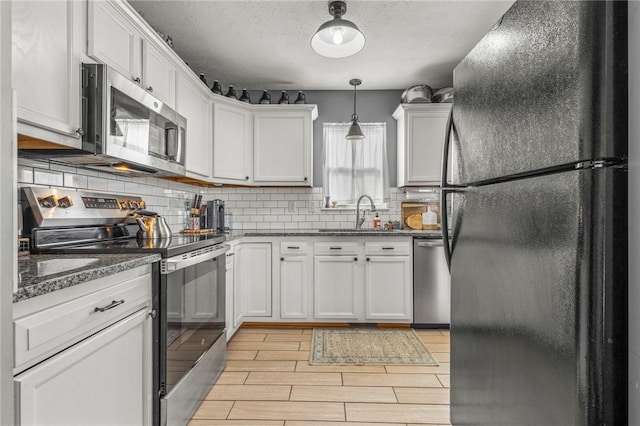 kitchen featuring white cabinetry, sink, decorative light fixtures, and appliances with stainless steel finishes