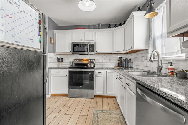 kitchen with sink, white cabinets, hanging light fixtures, light stone counters, and stainless steel appliances