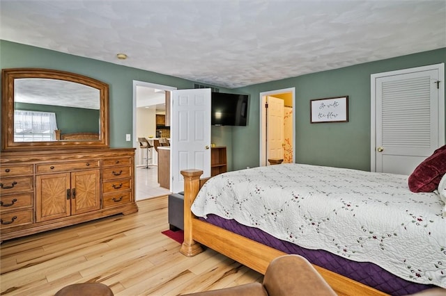 bedroom featuring light wood-type flooring, a textured ceiling, and ensuite bath