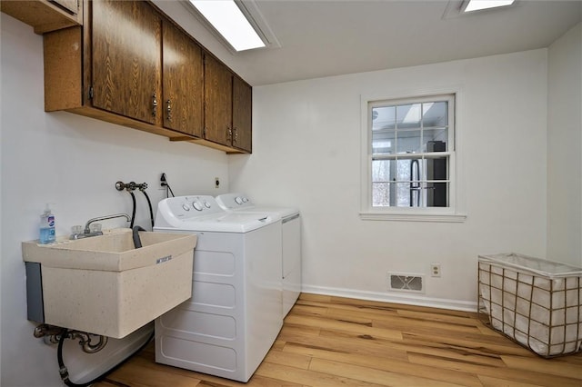 laundry area with light hardwood / wood-style flooring, sink, washer and clothes dryer, and cabinets