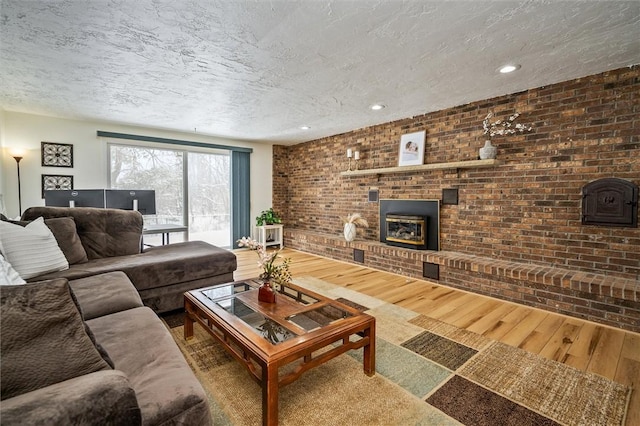 living room with brick wall, wood-type flooring, a brick fireplace, and a textured ceiling