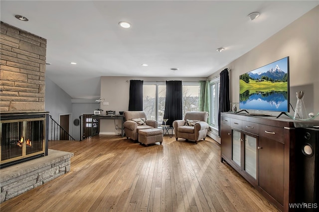 living room with a stone fireplace and light wood-type flooring