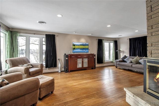 living room with a stone fireplace, a baseboard heating unit, and light hardwood / wood-style flooring